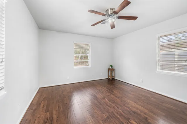 an empty room with wooden floor ceiling fan and windows