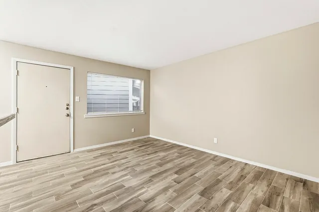 a view of an empty room with wooden floor and a window