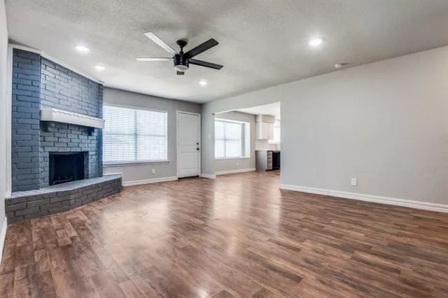 an empty room with wooden floor fireplace and windows