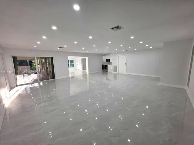a view of an empty room with wooden floor and kitchen
