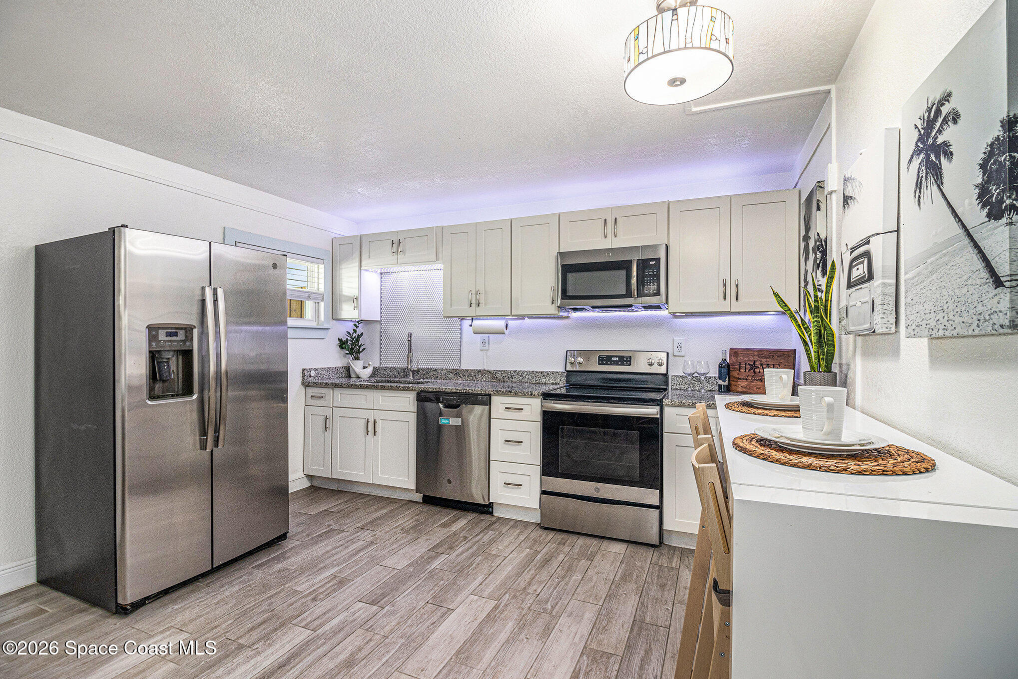 7605 Ridgewood Avenue, Unit 3 Cape Canaveral, FL 32920 - Photo 4 of 28 a kitchen with stainless steel appliances granite countertop a refrigerator a stove top oven a sink dishwasher and a refrigerator with wooden floor