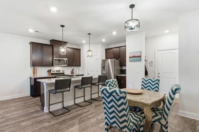 a kitchen with stainless steel appliances kitchen island granite countertop a dining table chairs and a refrigerator