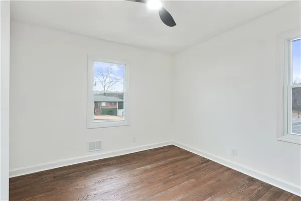 an empty room with wooden floor fan and windows