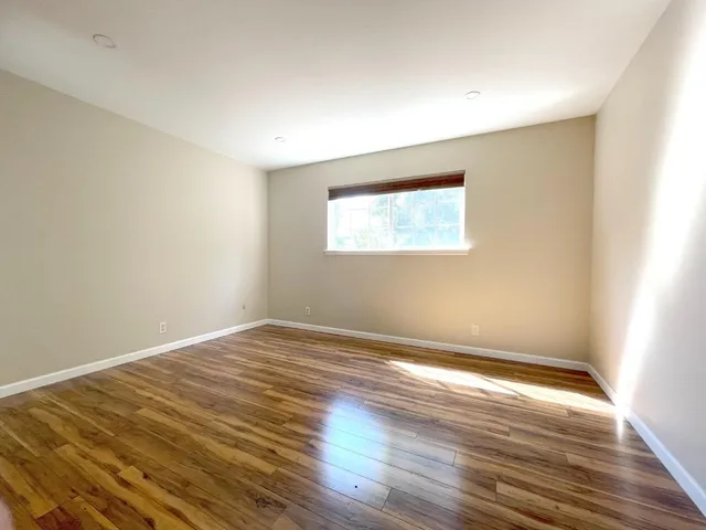 a view of an empty room with wooden floor and a window