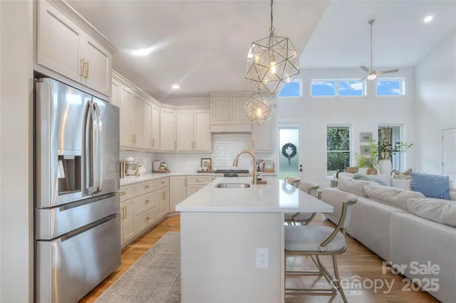 a kitchen with stainless steel appliances kitchen island granite countertop a refrigerator a sink dishwasher a dining table and chairs with wooden floor