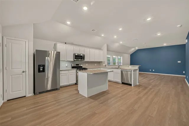 a kitchen with stainless steel appliances granite countertop a stove top oven a sink dishwasher and a refrigerator with wooden floor