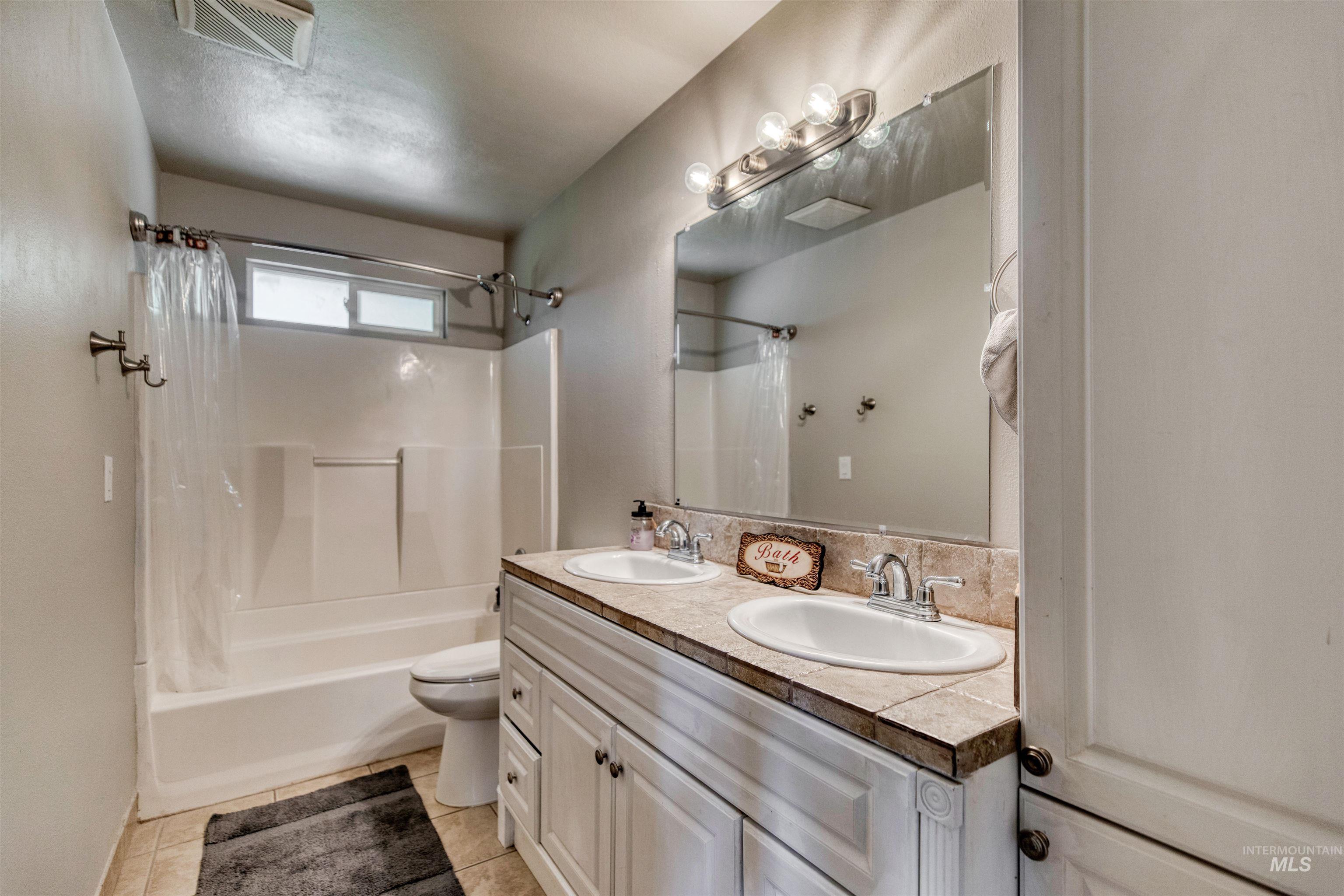 20803 Friends Road Greenleaf, ID 83626 - Photo 20 of 39 Bathroom featuring a dual vanity with undermount sinks, a tile countertop, a large mirror, and overhead vanity lighting