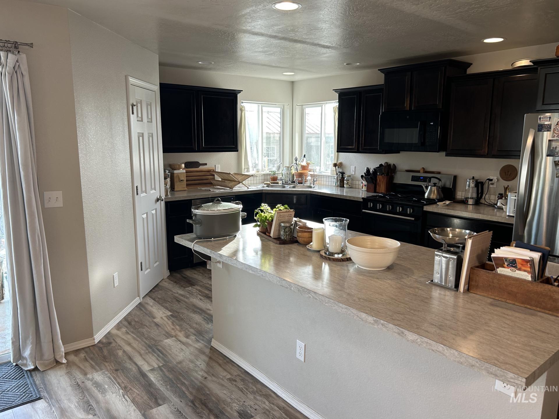 5614 Barkley Way Caldwell, ID 83607 - Photo 19 of 50 Kitchen featuring dark cabinets, gas stove, light countertops, black microwave, and freestanding refrigerator
