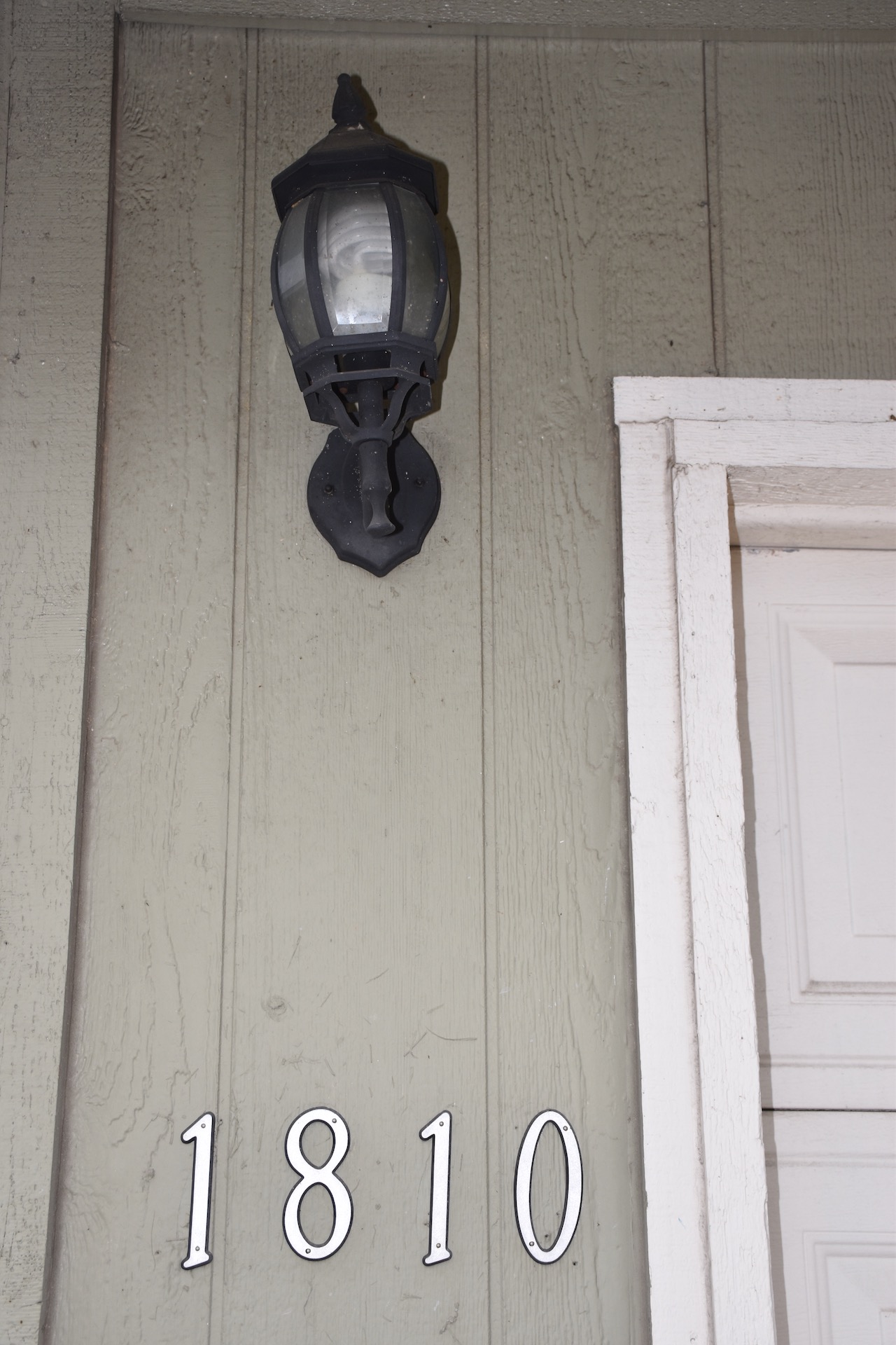 1810 Rawhide Loop Round Rock, TX 78681 - Photo 3 of 29 Vertical plank siding featuring a wall-mounted lantern light fixture with clear glass panes and a cast-iron finish