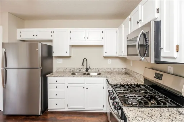 a kitchen with granite countertop a refrigerator stove and white cabinets
