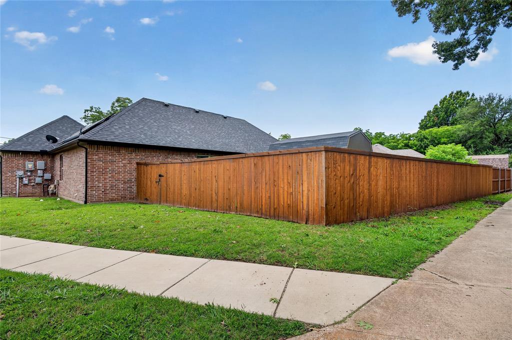 701 West Lamberth Road Sherman, TX 75092 - Photo 34 of 37 Property exterior featuring brick siding, a dark shingle roof, a wood privacy fence, a sidewalk, and a manicured lawn