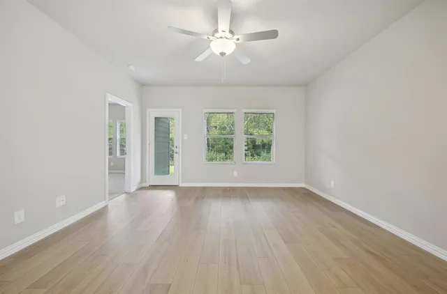 an empty room with wooden floor chandelier fan and windows