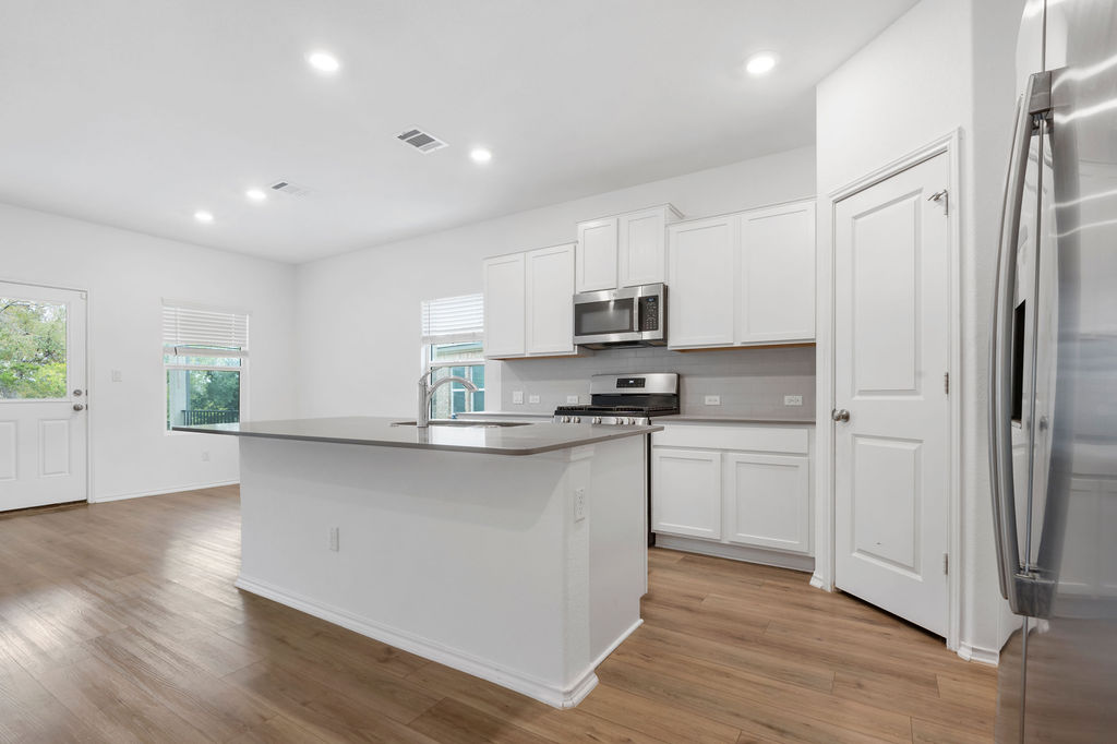 1205 Sweetspire Street Leander, TX 78641 - Photo 6 of 31 Kitchen with appliances with stainless steel finishes, recessed lighting, white cabinets, a kitchen island with sink, and decorative backsplash