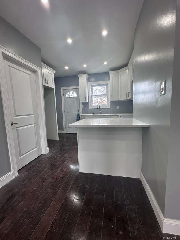 114-06 Inwood Street Queens, NY 11436 - Photo 2 of 18 Kitchen with a peninsula, white cabinets, dark wood-style flooring, a breakfast bar area, and light stone countertops