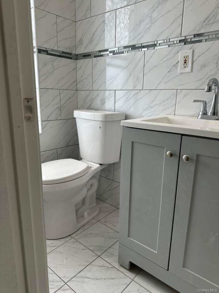 114-06 Inwood Street Queens, NY 11436 - Photo 3 of 18 Bathroom featuring vanity, tile walls, and light marble finish flooring