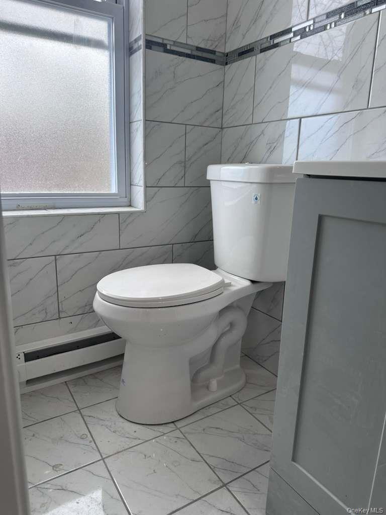 114-06 Inwood Street Queens, NY 11436 - Photo 10 of 18 Half bathroom featuring tile walls, light marble finish flooring, and a baseboard radiator