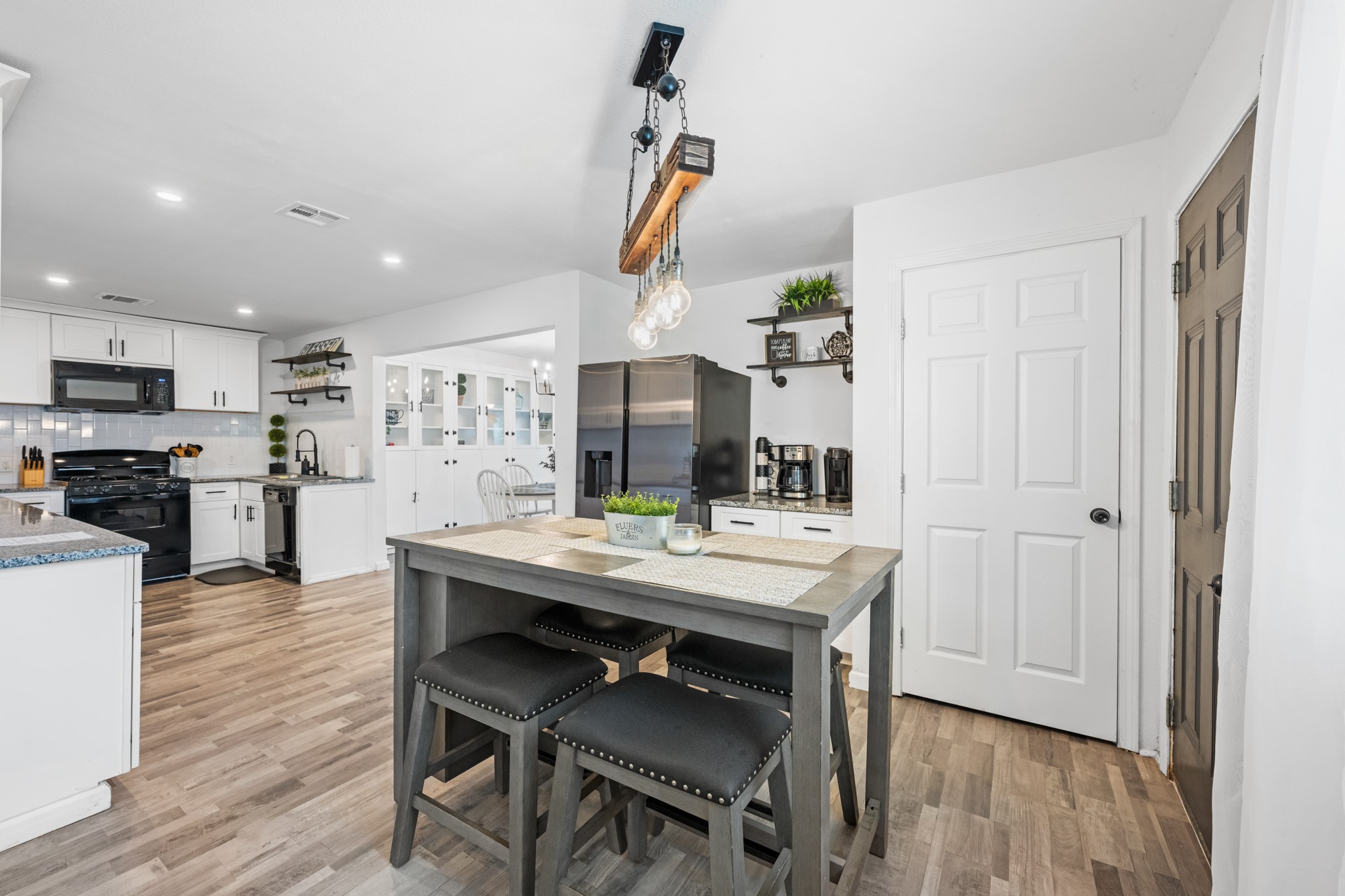 729 Kyle Angleton, TX 77515 - Photo 14 of 36 Modern kitchen with open layout, featuring white cabinets, stainless steel appliances, and a stylish island with seating. The space is bright and inviting, with wood-look flooring and contemporary lighting.