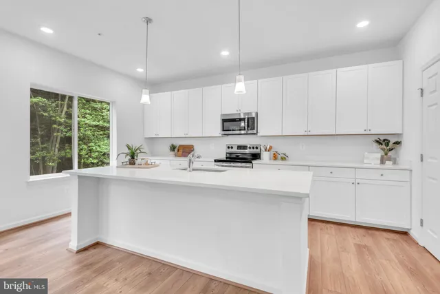 a kitchen with stainless steel appliances granite countertop a sink a stove a refrigerator and white cabinets with wooden floor