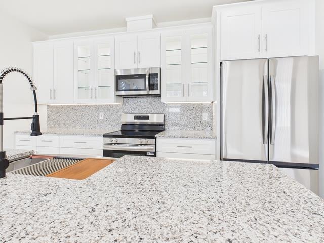 511 Richardson Street Athens, TX 75751 - Photo 11 of 40 Kitchen with stainless steel appliances, light stone countertops, backsplash, and glass insert cabinets