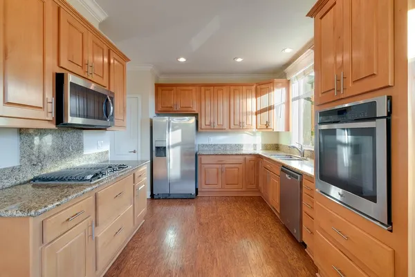 a kitchen with stainless steel appliances granite countertop a sink a stove a refrigerator cabinets and a wooden floor