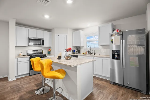 a kitchen with stainless steel appliances granite countertop a refrigerator a stove top oven a dining table and chairs with wooden floor