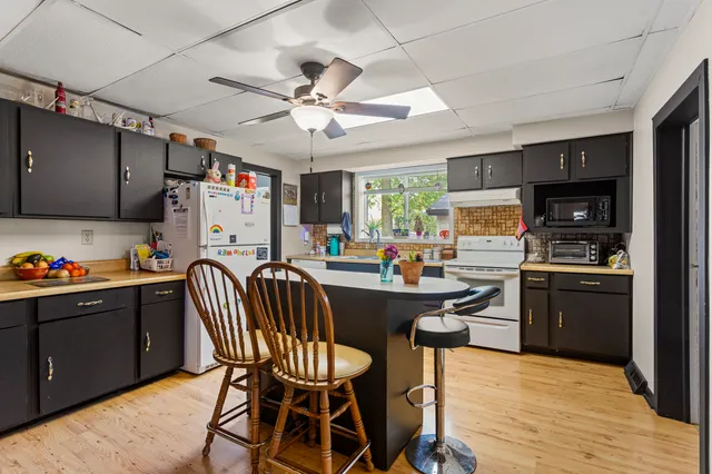 a kitchen with stainless steel appliances kitchen island granite countertop a refrigerator a stove top oven a sink dishwasher and a dining table with wooden floor