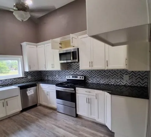 a white kitchen with granite countertop a stove and a sink