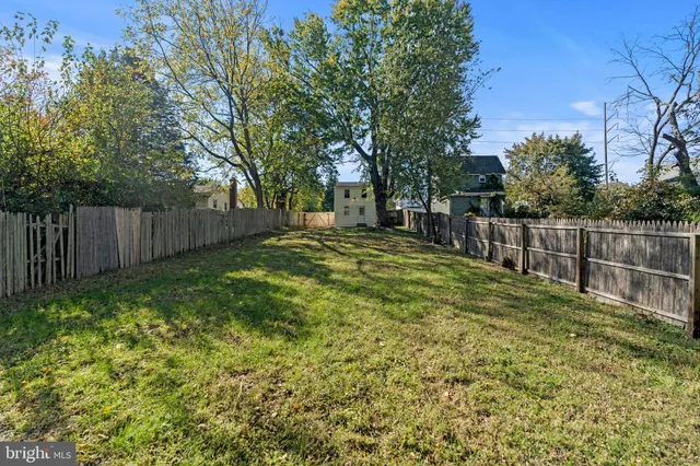 a view of a backyard with wooden fence and large trees