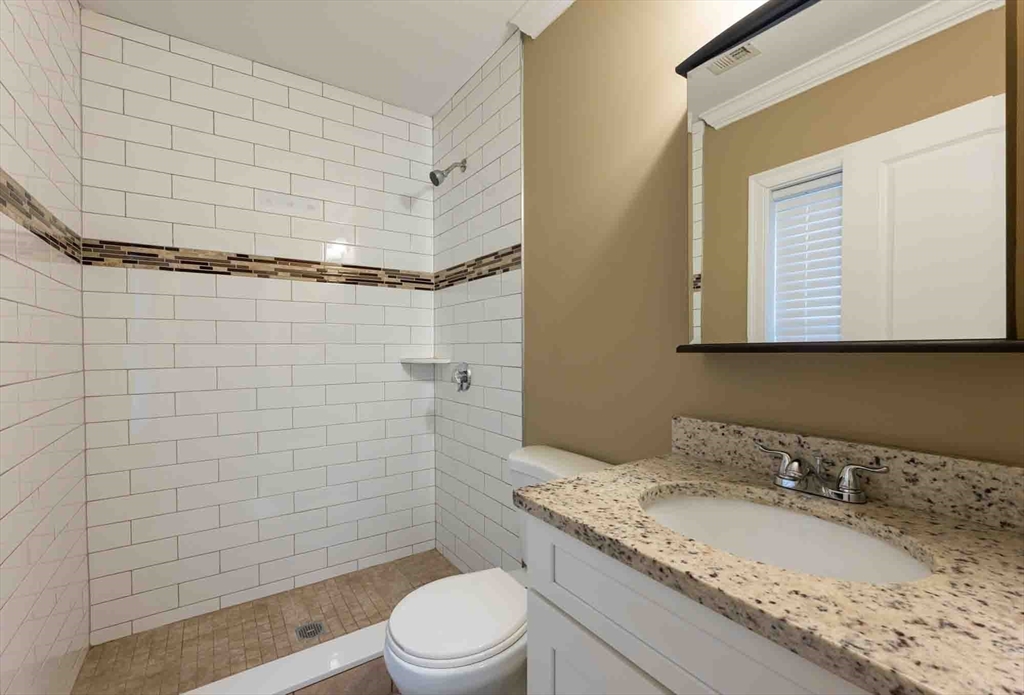 51 Branch Street, Unit 2 Quincy, MA 02169 - Photo 31 of 37 a bathroom with a granite countertop sink toilet a mirror and shower