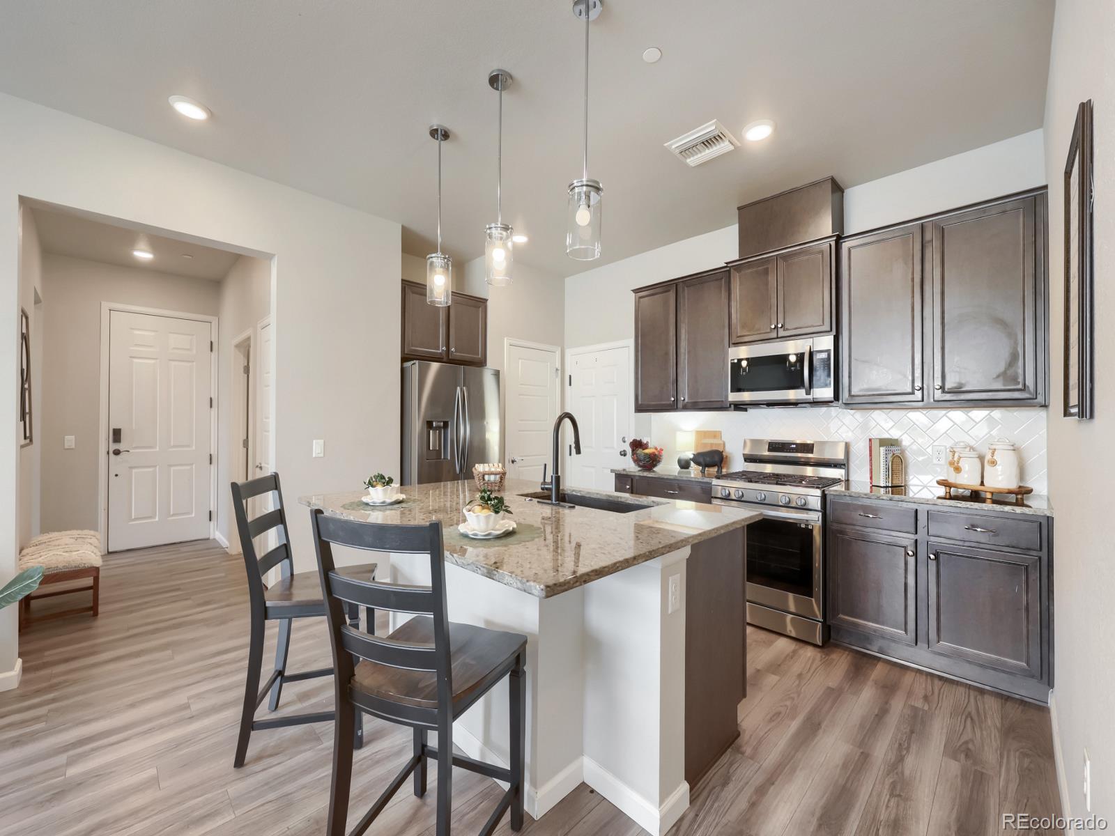 6153 North Ceylon Street, Unit 10108 Denver, CO 80249 - Photo 4 of 11 a kitchen with stainless steel appliances granite countertop a kitchen island hardwood floor sink stove dining table and chairs
