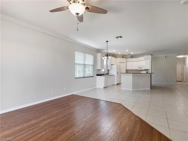 an empty room with wooden floor kitchen view and windows