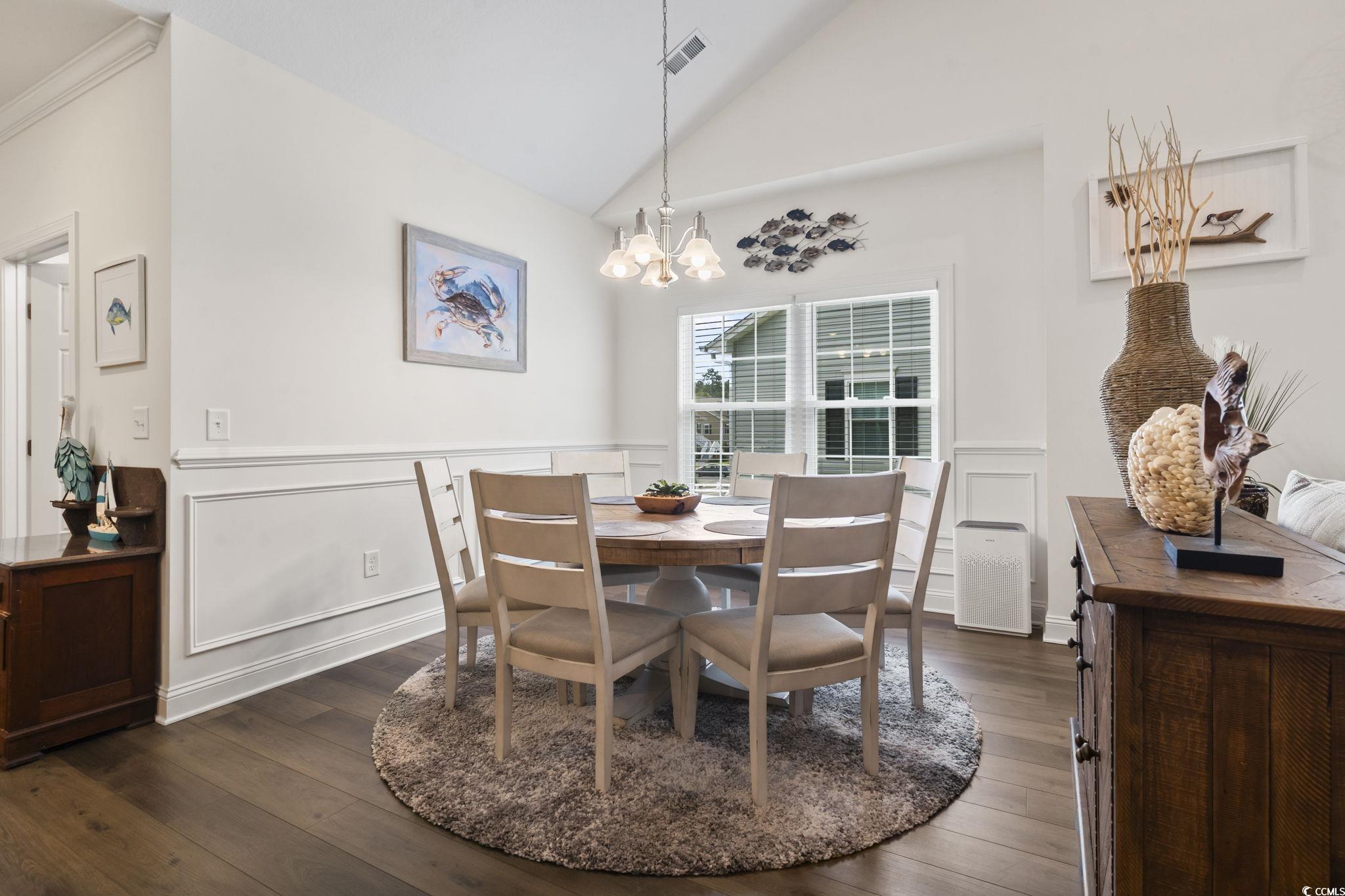 924 Jackline Place, Unit 201 Murrells Inlet, SC 29576 - Photo 13 of 35 Dining area with dark wood-style flooring, a decorative wall, wainscoting, a chandelier, and high vaulted ceiling