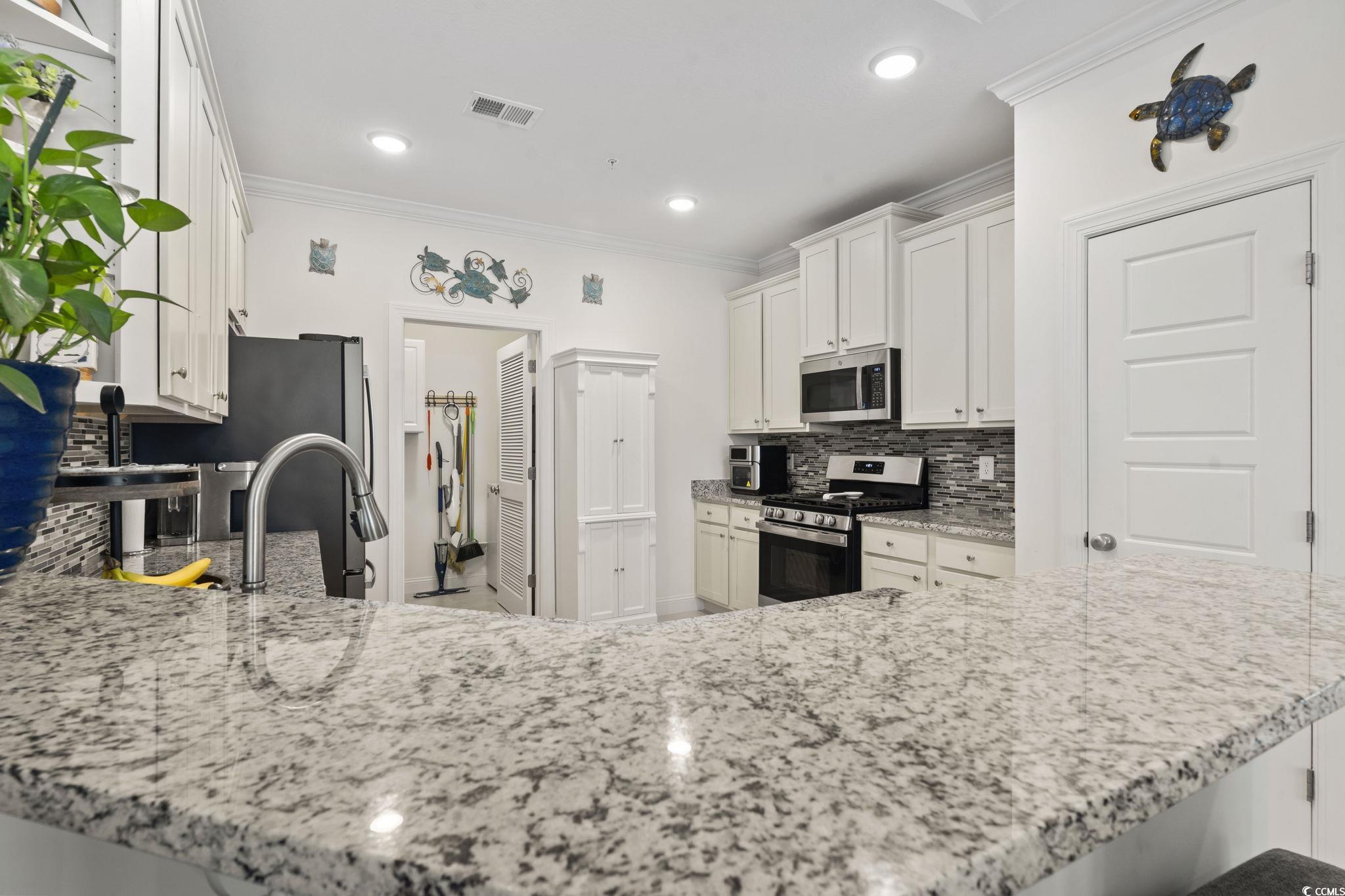 924 Jackline Place, Unit 201 Murrells Inlet, SC 29576 - Photo 8 of 35 Kitchen with decorative backsplash, white cabinetry, crown molding, light stone counters, and stainless steel appliances