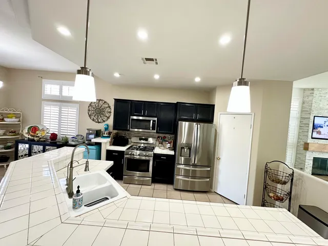 a kitchen with stainless steel appliances kitchen island granite countertop a refrigerator a stove a sink dishwasher a dining table and chairs with wooden floor
