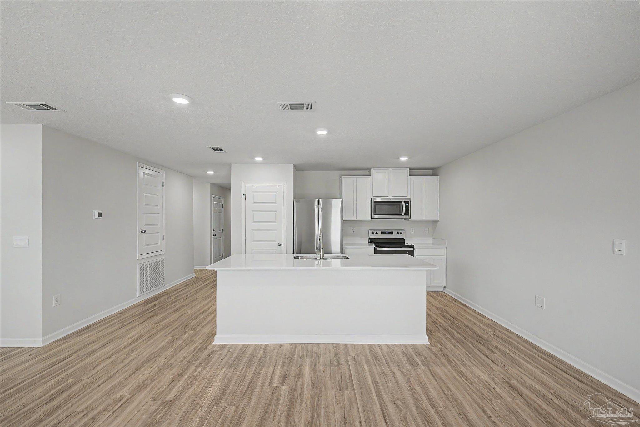 2665 Saltgrass Way Crestview, FL 32536 - Photo 7 of 22 a large kitchen with kitchen island a stove a refrigerator white cabinets and wooden floor