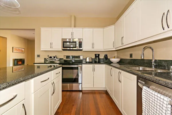 a kitchen with stainless steel appliances granite countertop a sink a stove top oven a refrigerator with white cabinets and black appliances