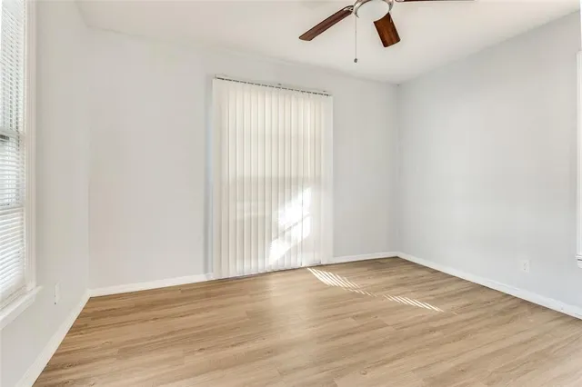 an empty room with wooden floor fan and windows