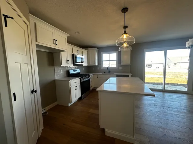 a kitchen with stainless steel appliances granite countertop a refrigerator a sink dishwasher a stove and a dining table with wooden floor