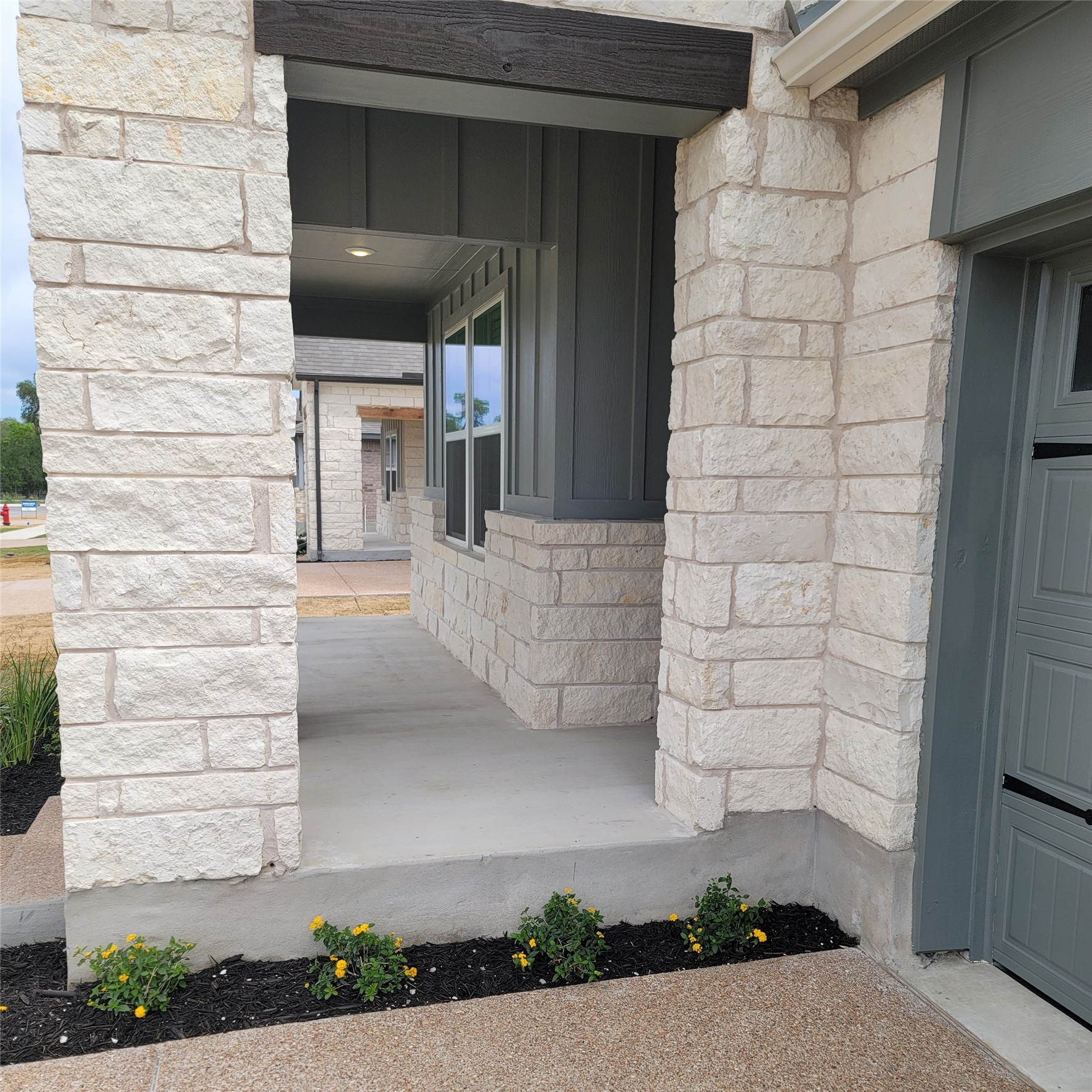 200 Callahan Loop Buda, TX 78610 - Photo 2 of 13 Front entryway featuring light-toned stone construction, a dark gray board-and-batten accent wall, a wood-finish beam, recessed lighting, and a concrete patio