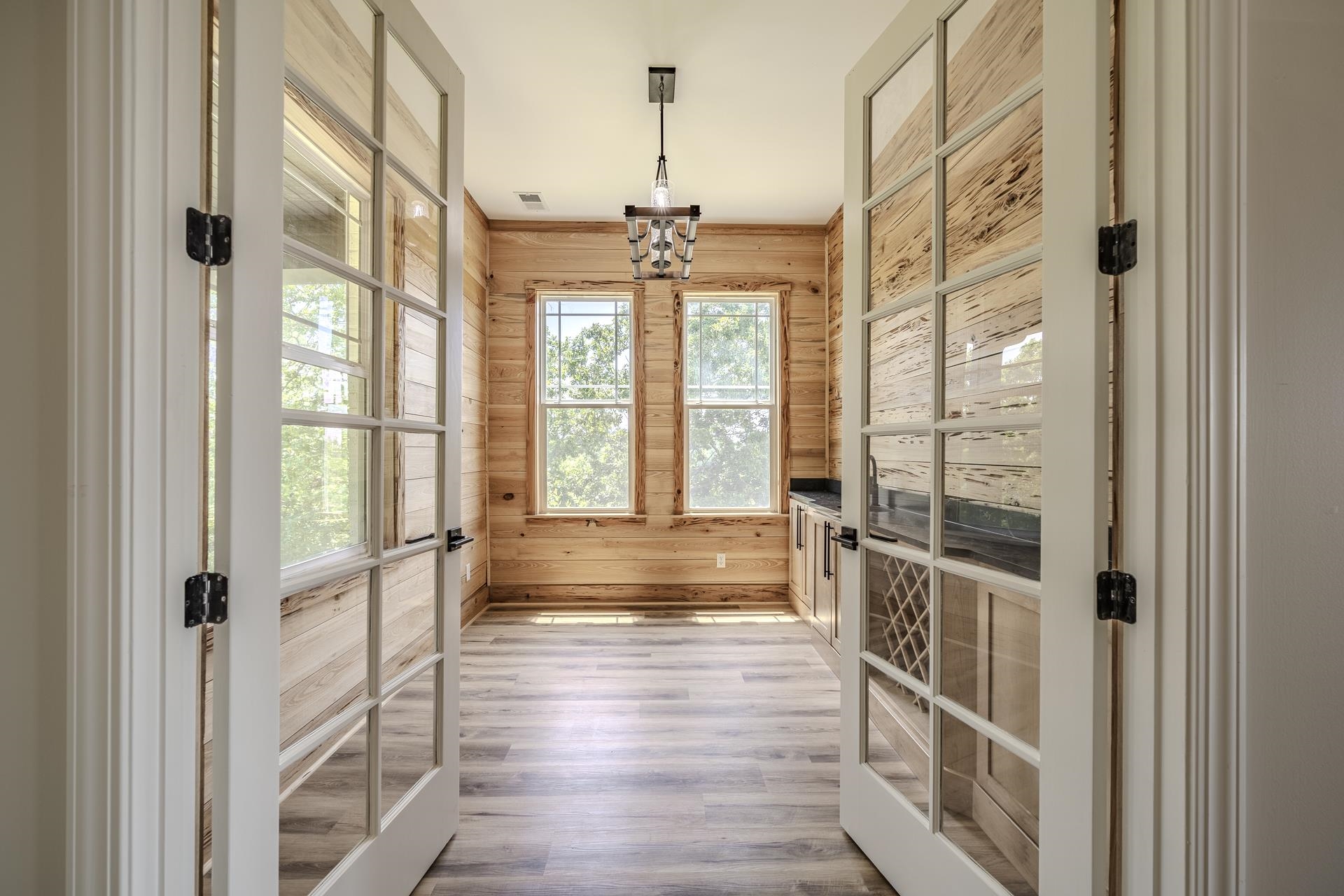 851 Rivers Edge Drive Bath Springs, TN 38311 - Photo 12 of 39 Double French doors opening to an interior room with wood plank walls, light wood-finish flooring, two large windows, and built-in cabinetry with a dark countertop and wine rack