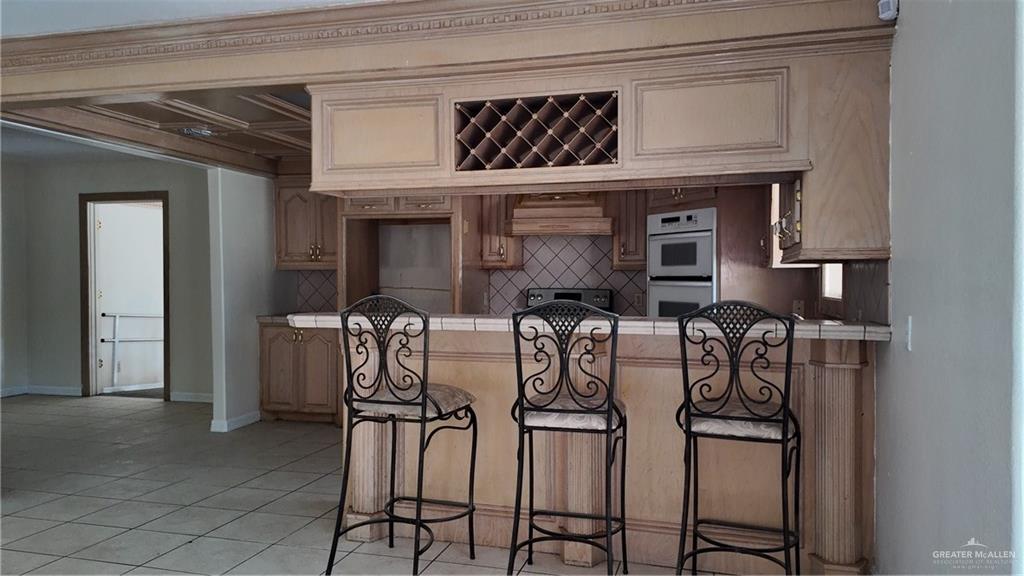 612 West Ramirez Street Rio Grande City, TX 78582 - Photo 19 of 40 Kitchen featuring tile counters, multiple ovens, extractor fan, a breakfast bar, and coffered ceiling
