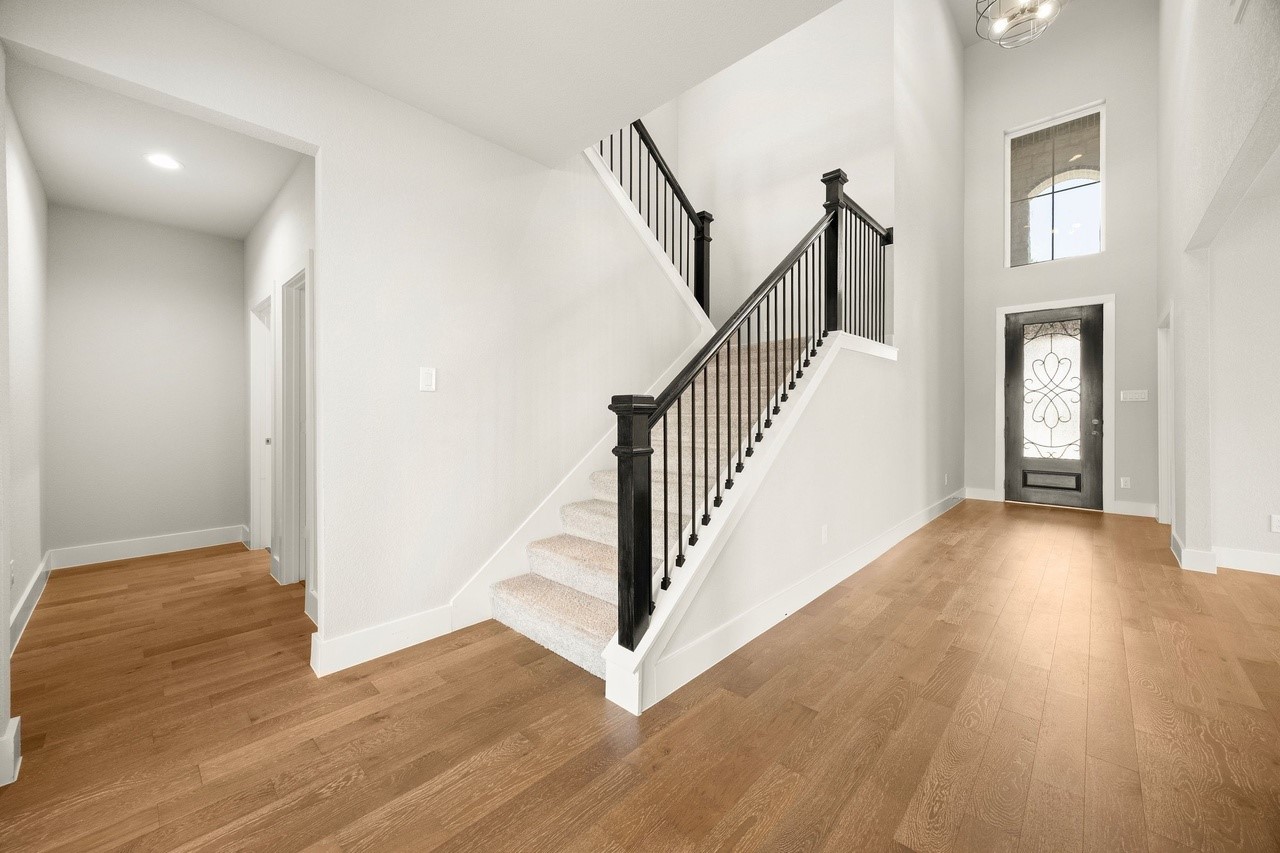 A grand entryway with elegant hardwood floors and a striking staircase featuring sleek black railings, leading to a bright and open space filled with natural light.
