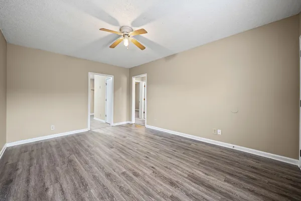 a view of an empty room with wooden floor and a ceiling fan