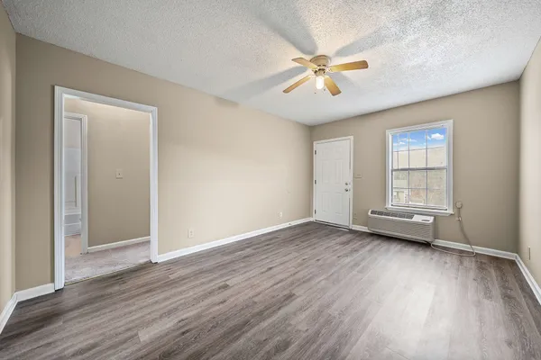 an empty room with wooden floor fan and windows