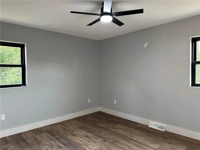 an empty room with wooden floor fan and windows