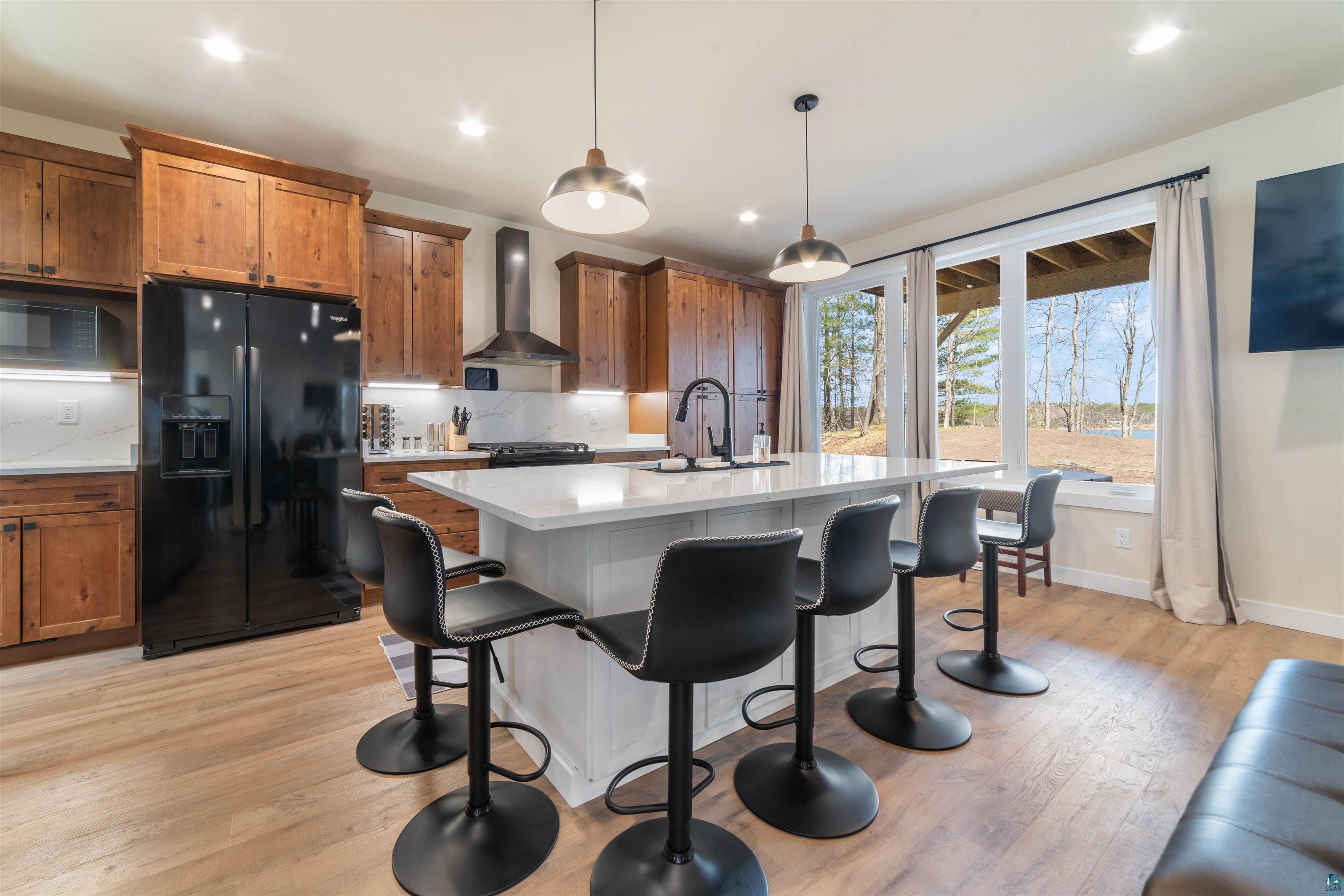 2000 West Chub Lake Road Carlton, MN 55718 - Photo 10 of 30 Open-concept kitchen featuring wood-finish cabinetry, a large center island with seating, a black side-by-side refrigerator, and a stainless steel range hood