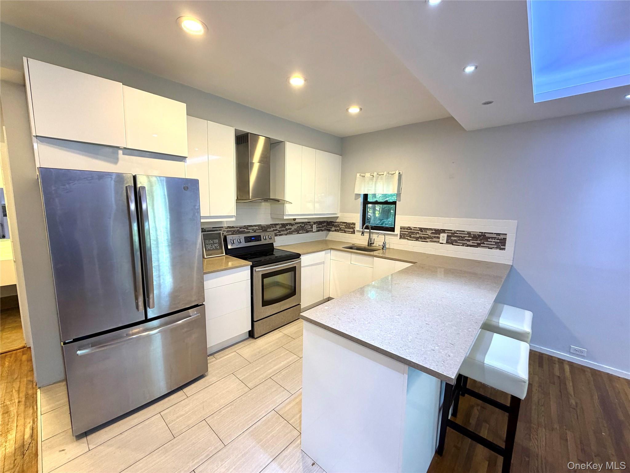 77 Sands Point Road, Unit #1 Port Washington, NY 11050 - Photo 3 of 19 Modern kitchen featuring stainless steel appliances, white cabinetry, a light-colored countertop, and a tiled backsplash