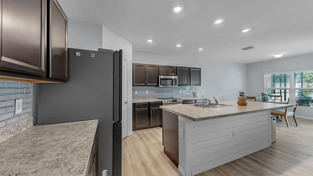 14530 Haddon Mist Drive Wimauma, FL 33598 - Photo 6 of 44 a kitchen with stainless steel appliances granite countertop a stove top oven a sink dishwasher a refrigerator and a dining table with wooden floor