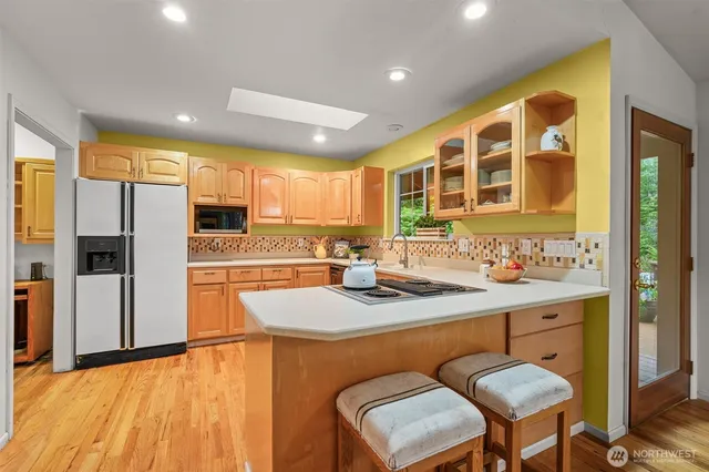 a kitchen with stainless steel appliances granite countertop a sink a stove a refrigerator cabinets and a dining table with wooden floor