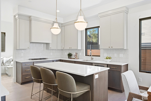 4092 Discovery Way Park City, UT 84098 - Photo 13 of 66 Modern kitchen featuring white shaker upper cabinetry and dark wood-finish lower cabinetry, a center island with seating, a gas range, and a tile backsplash